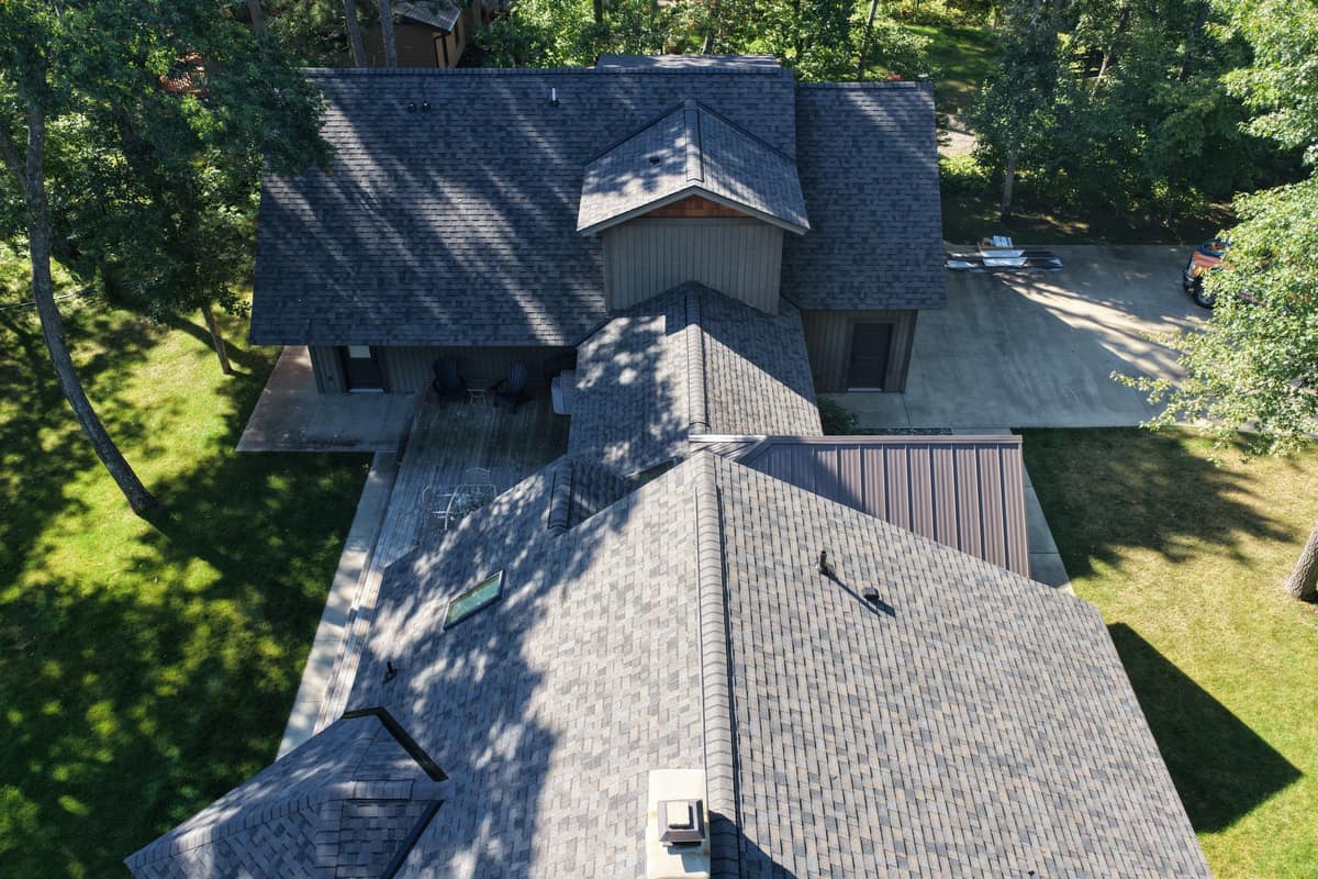 Drone view of a new gray architectural shingle roof with a skylight and metal accent roof on a lake-area home in Crosslake, MN