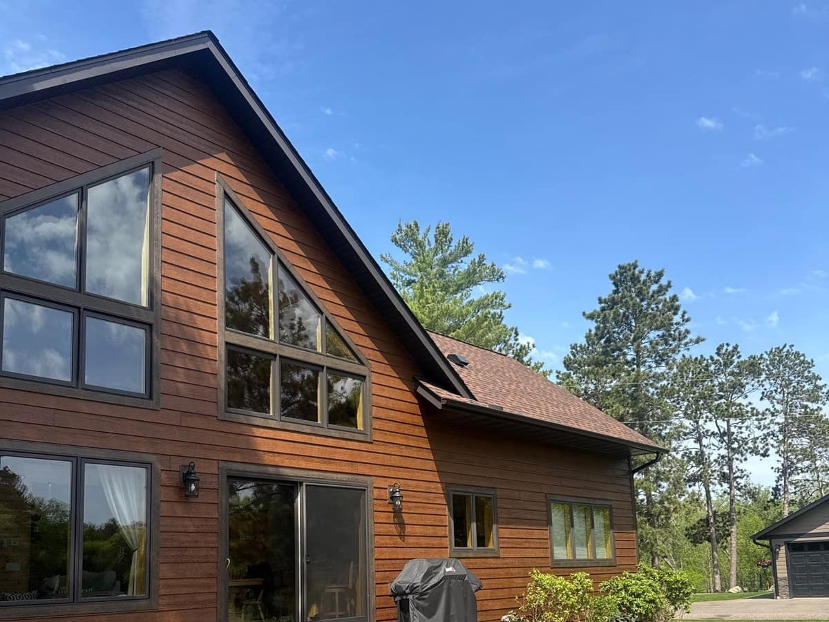 New cedar-tone siding and a new shingle roof on a lake home with large gable windows in Crosslake, MN