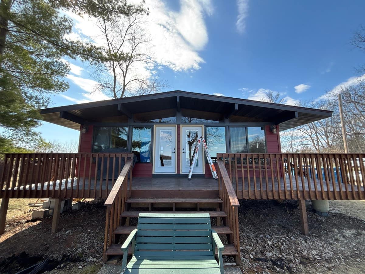 Cabin with red siding, dark soffit and a wood deck in Paynesville, MN