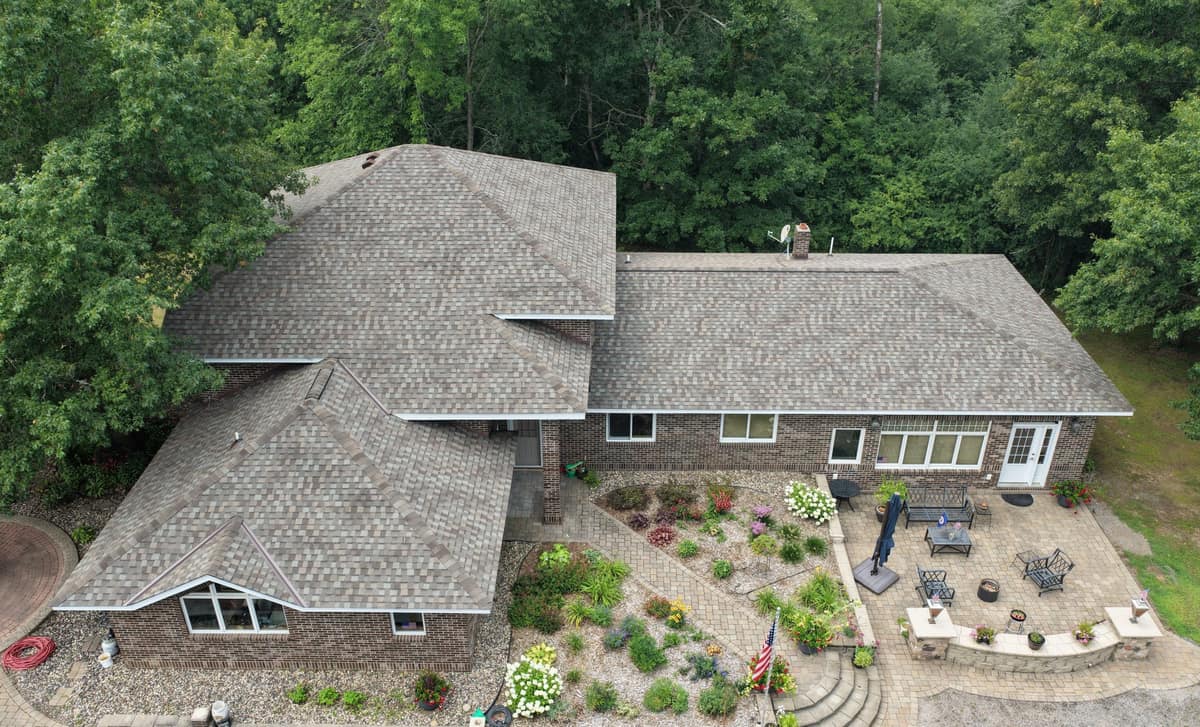 Drone view of a new shingle roof on a brick home with a paver patio in St. Augusta, MN