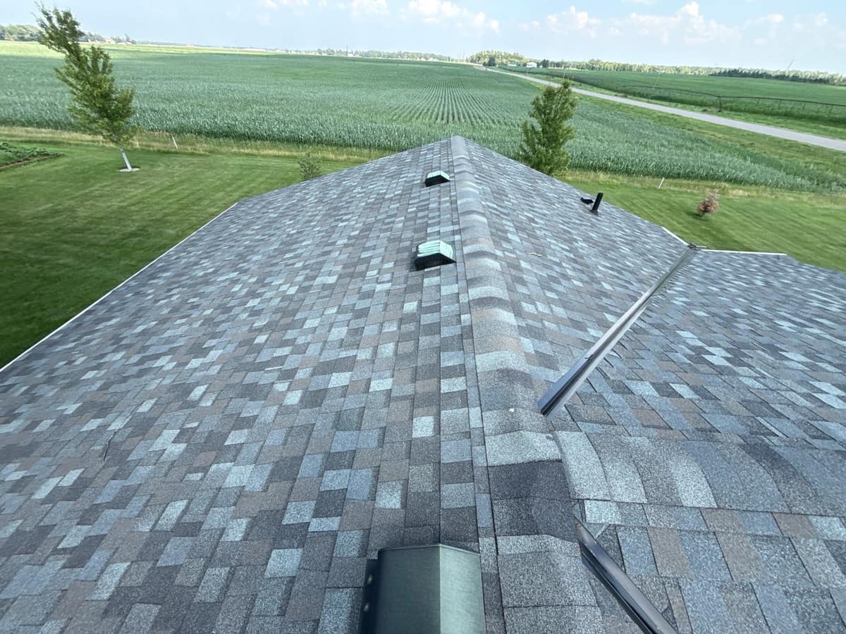New gray architectural shingle roof with ridge vents on a home beside farm fields in St. Joseph, MN
