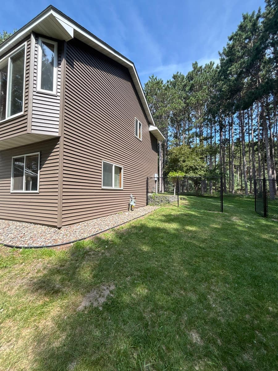 Corner of a two-story Big Lake, MN home with new deep brown vinyl siding among tall pines