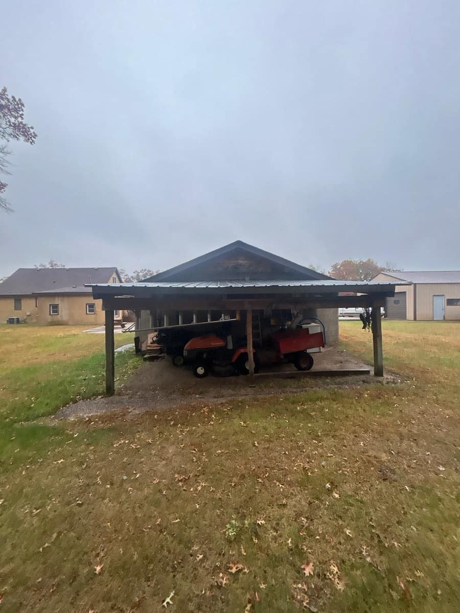 Open-sided lean-to shelter on the gable end of the stucco building in Brainerd, with the new shingle roof behind it