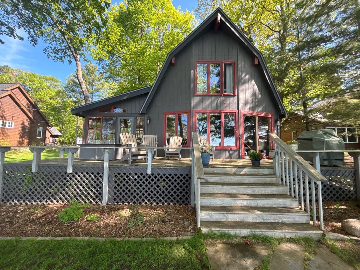 Lake side of a gambrel-roof cottage in Crosslake with red trim, deck stairs and a new charcoal shingle roof