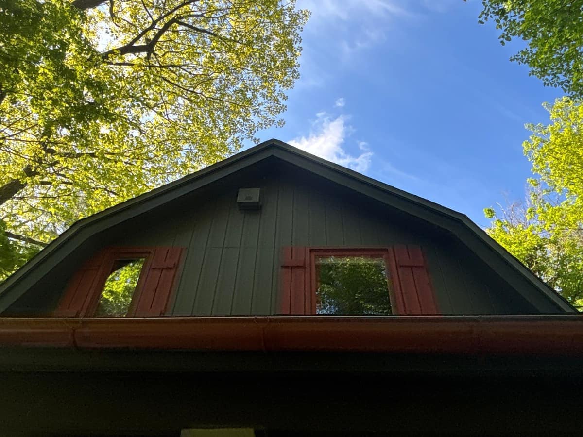 Gambrel gable with red shutters and a gutter below the new roof in Crosslake