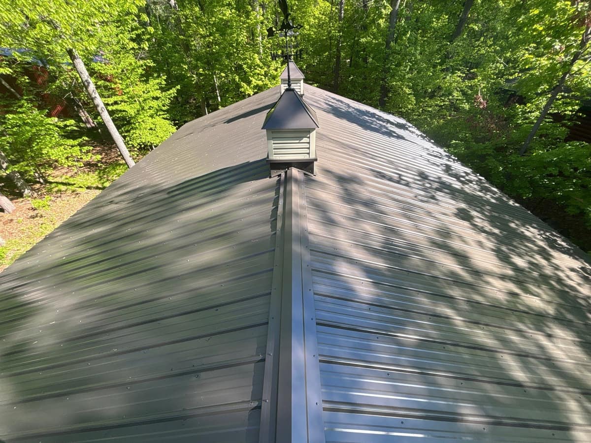 Dark green steel hip roof with a cupola on an outbuilding in Crosslake
