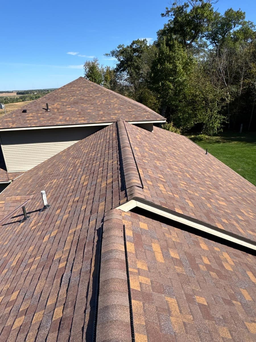 Roof sections meeting at a valley on the new brown shingle roof, looking toward fields in Kimball