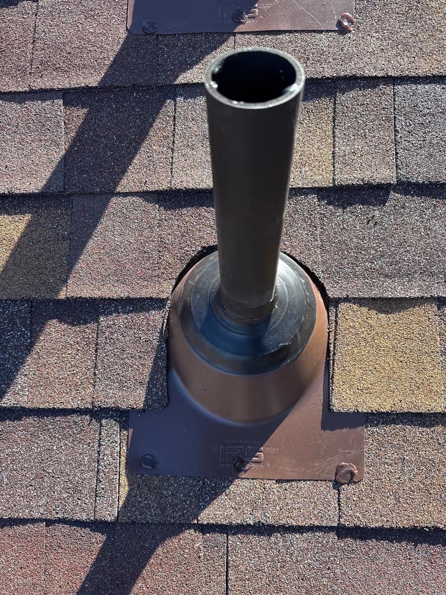 Plumbing vent pipe on a flanged boot set into the new brown shingles in Kimball