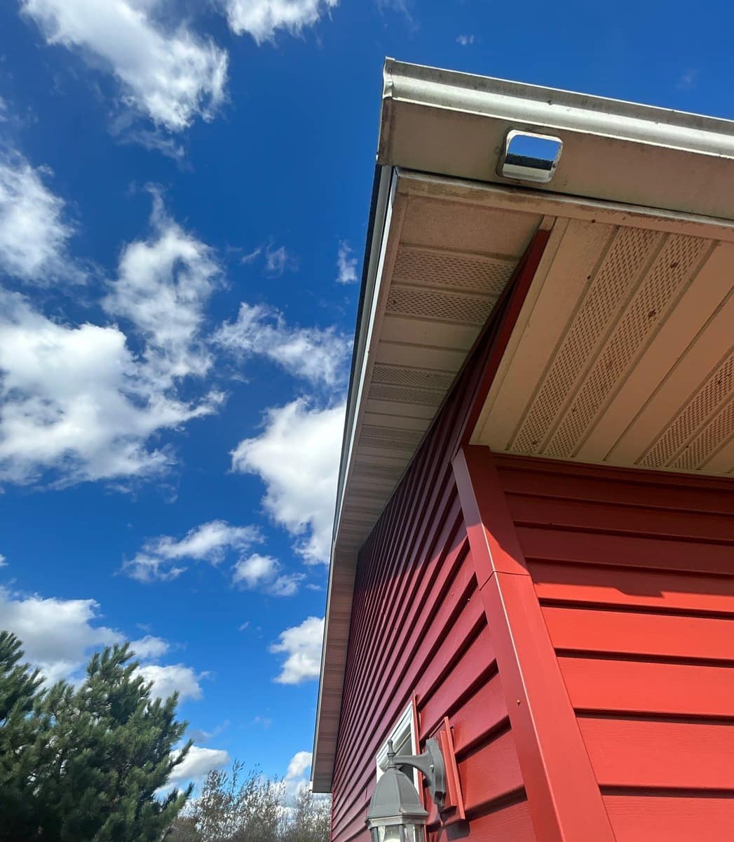 New gutter and vented soffit above red siding at a corner of the Milaca home