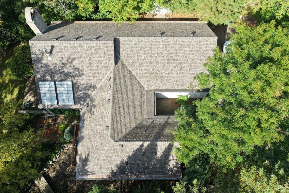 Overhead drone view of a finished shingle roof with skylights on a wooded lot in Minnetonka, MN