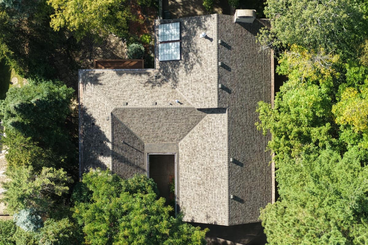 Drone view of the full Minnetonka roof showing new shingles, vents and skylights among trees
