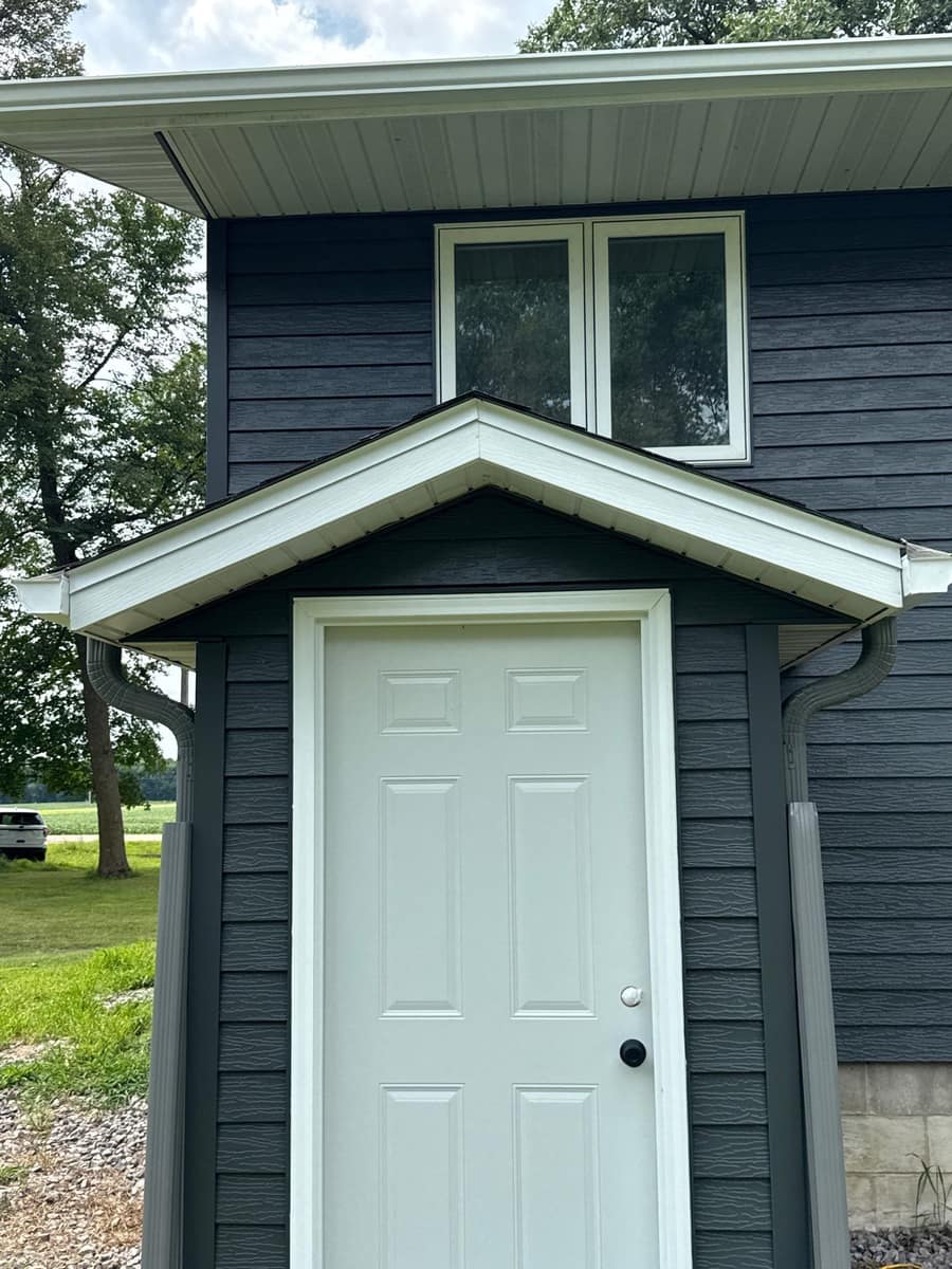 Back entry door under a small gable roof with new dark siding in Paynesville