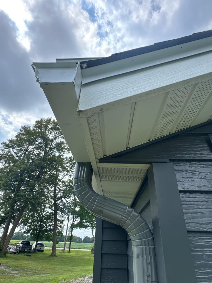 New gutter and gray downspout at a corner under white vented soffit in Paynesville