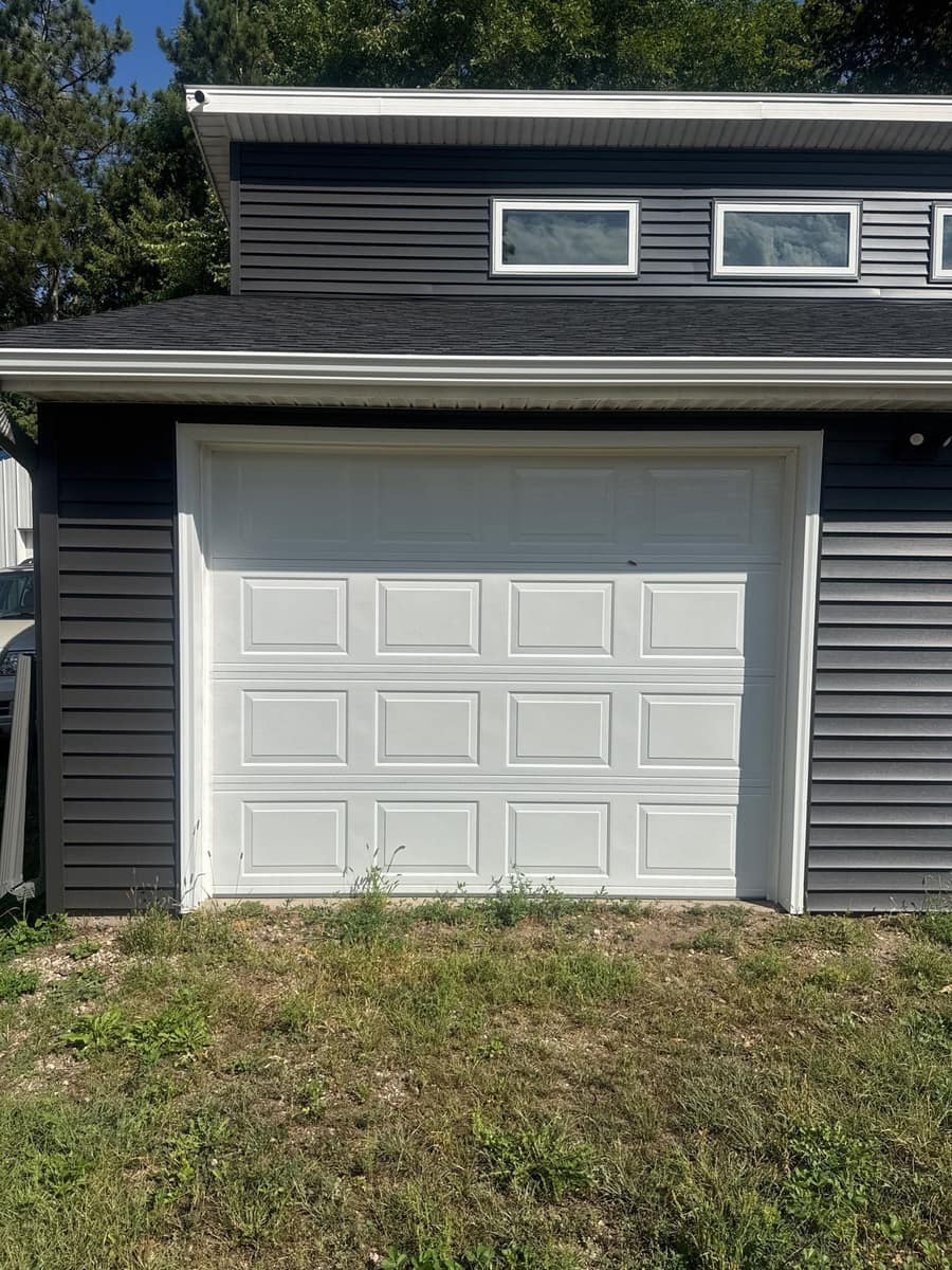Detached garage with a white wrapped overhead door and new gray siding in Paynesville, MN