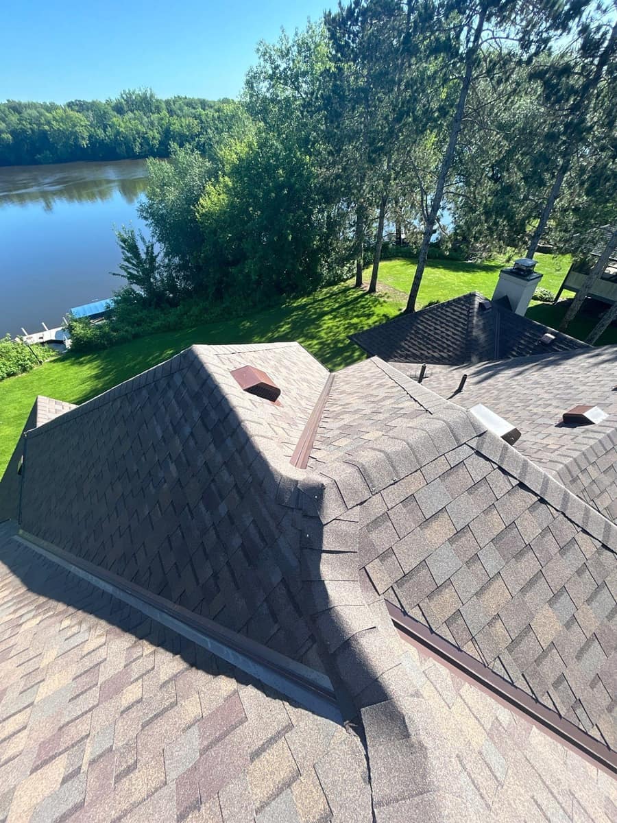 New shingles and roof vents around a chimney with the river in the background in Sartell