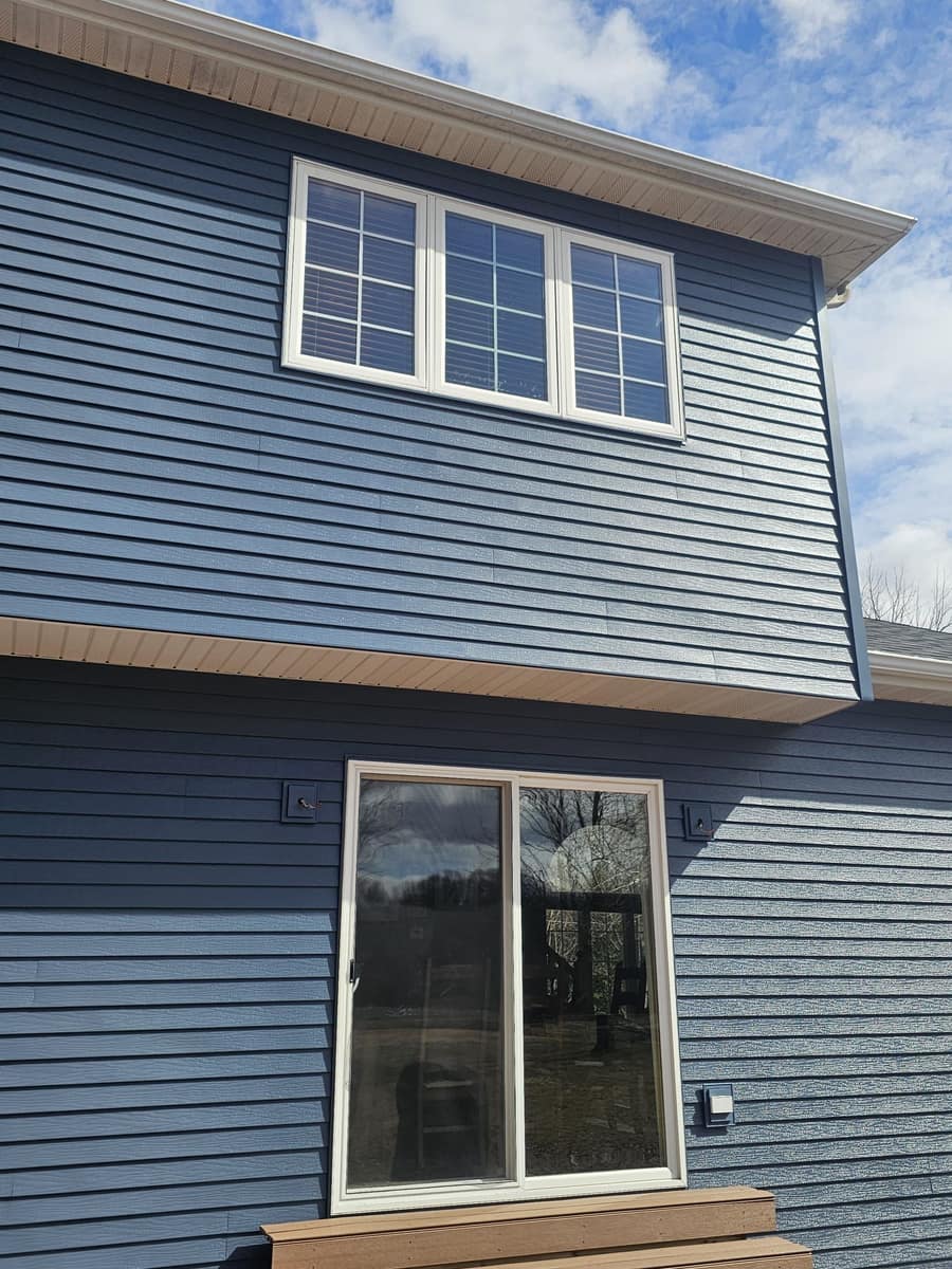 Rear of the Sartell home with new blue siding around a patio door and windows