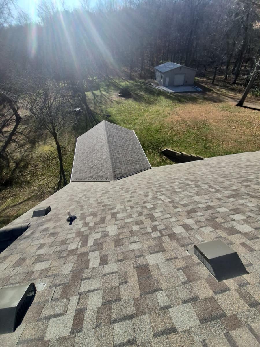New tan shingles with box vents near the peak, looking toward the steel garage in St. Augusta