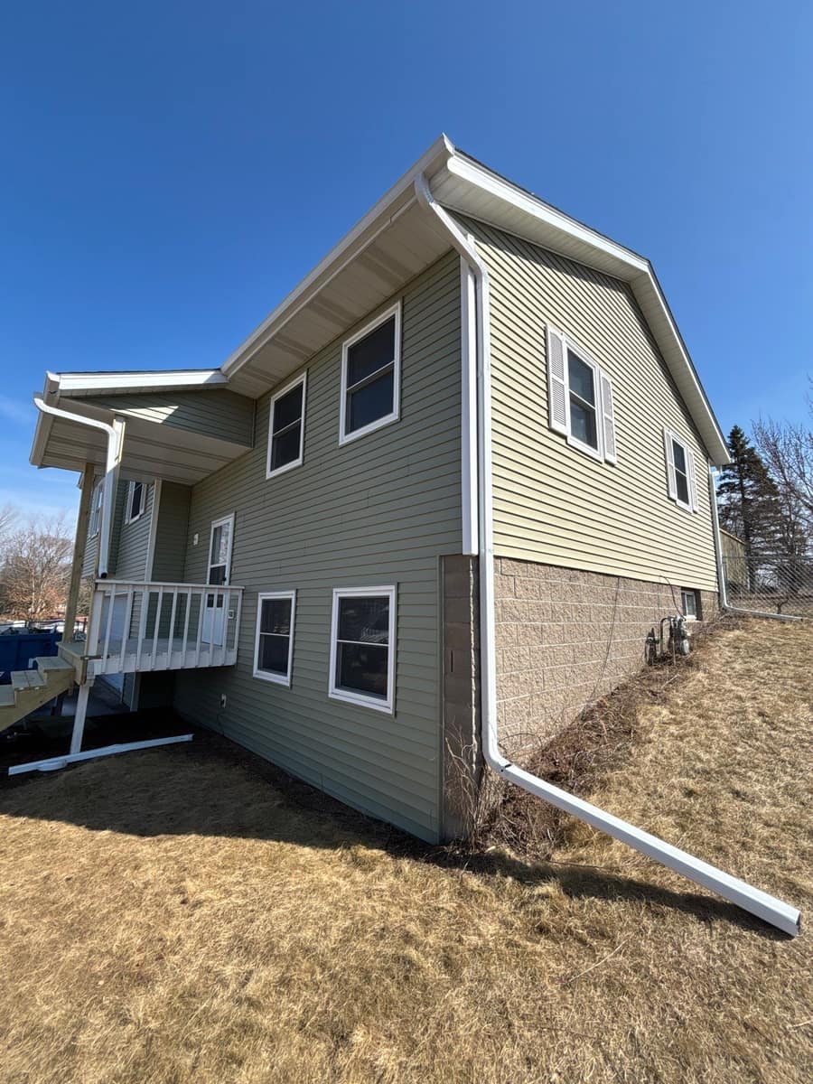 Corner of the St. Joseph home showing new green siding, white trim and a white downspout over the walkout level