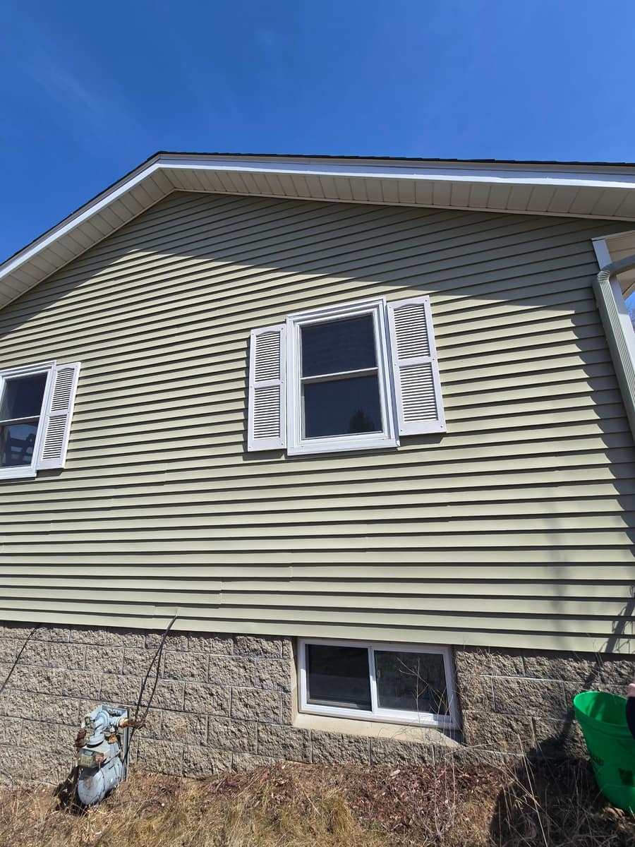 Close view of new green lap siding and a shuttered window above the block foundation in St. Joseph